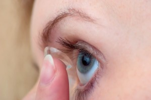 Woman inserting a corrective contact lens in blue eye